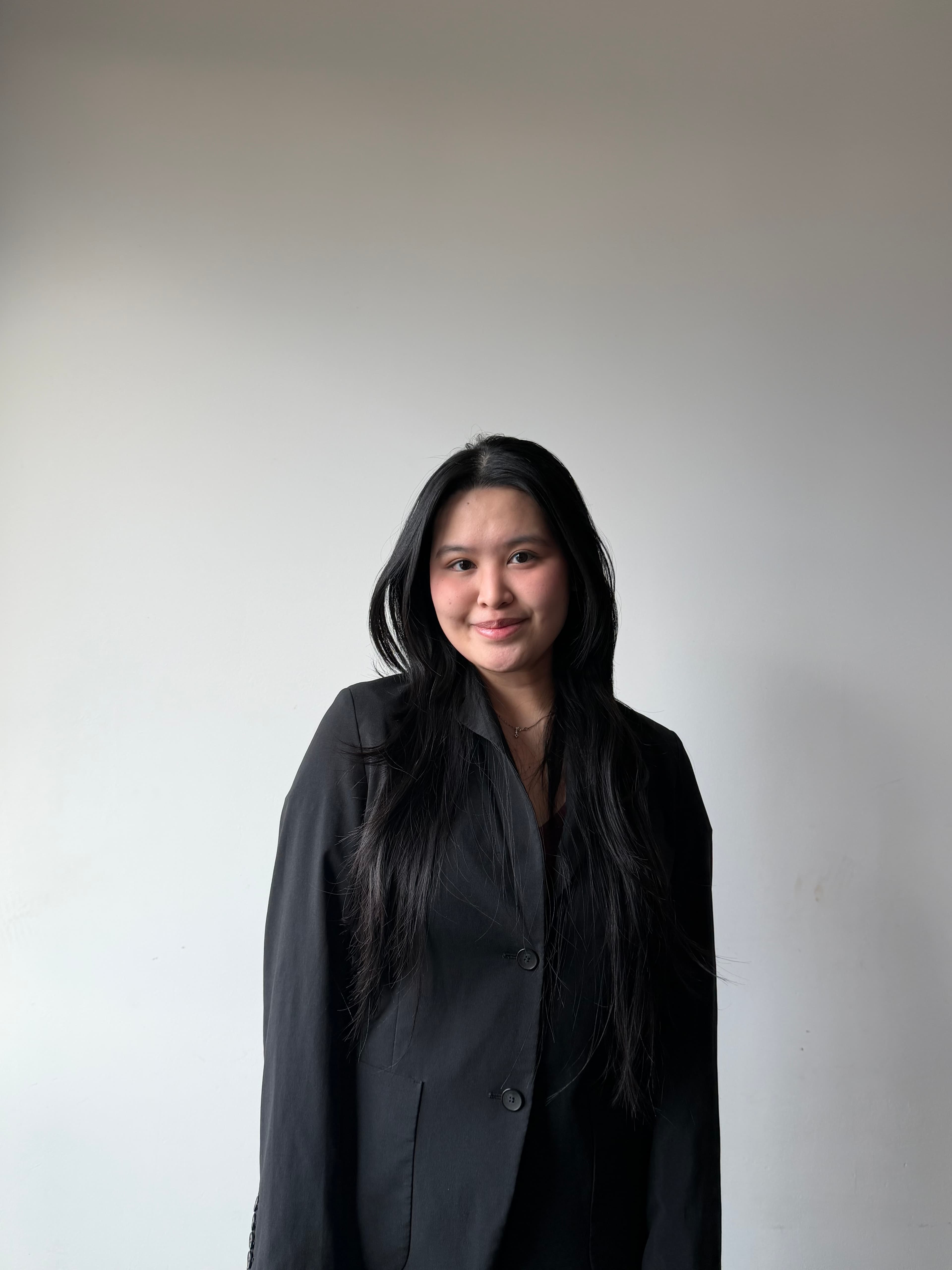 Smiling woman with long black hair wearing a black blazer against a neutral background.