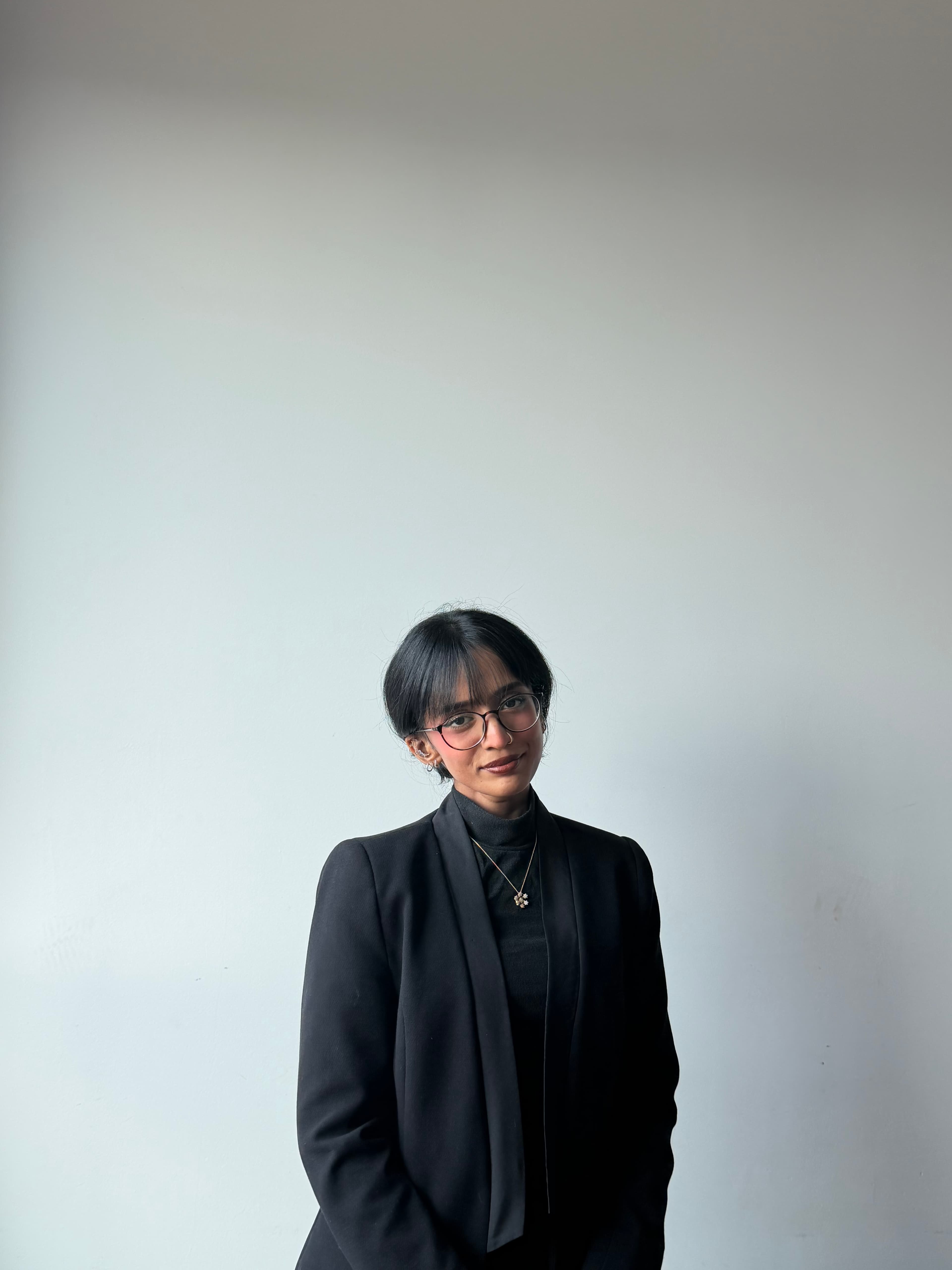 Young woman with short black hair and glasses wearing a black blazer and turtleneck sweater.